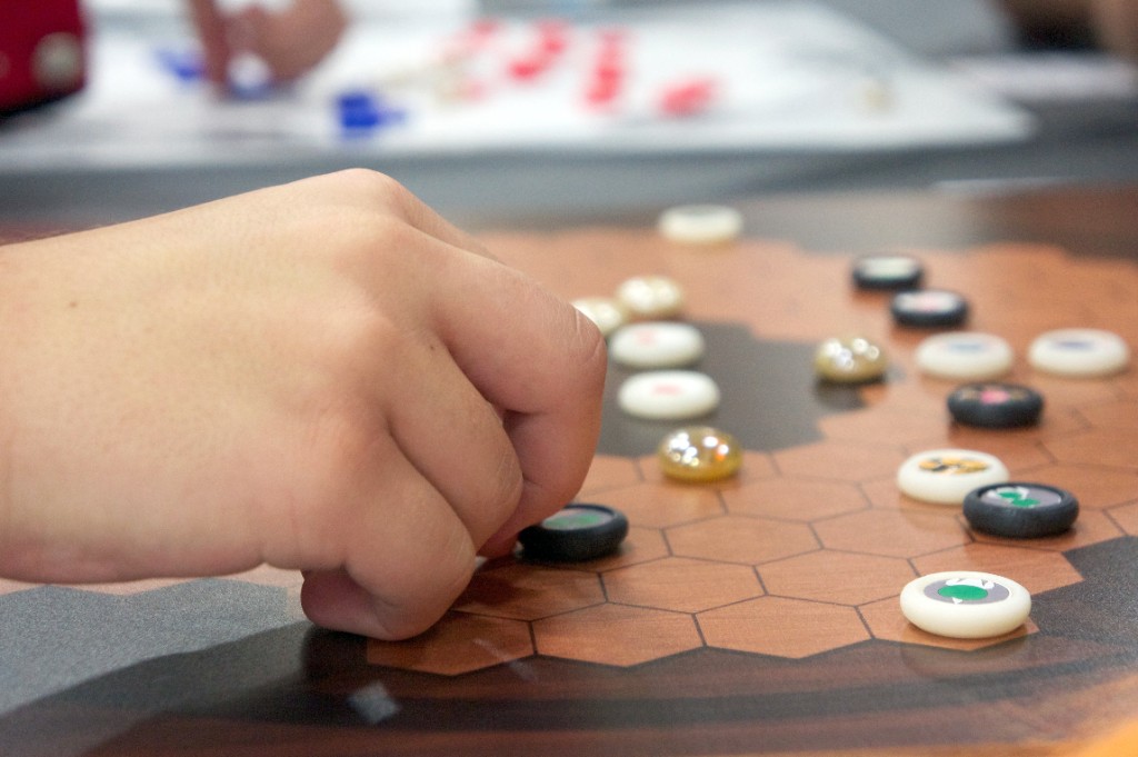 Close-up of a hand placing a piece on the wooden Enso Koi board during play.